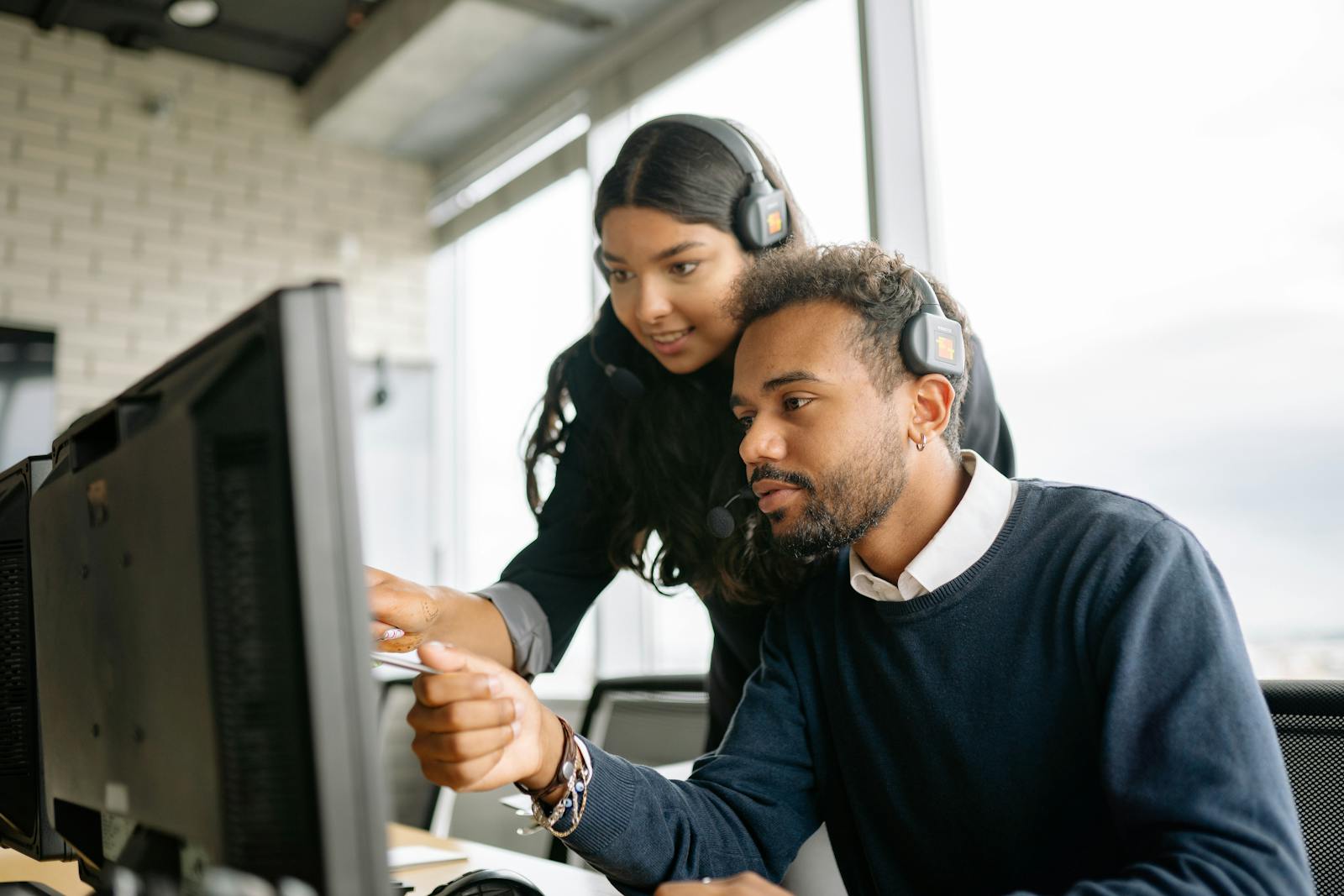 Two call center employees working together with headsets in a modern office setting.