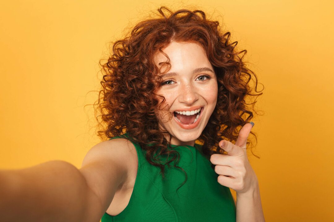 a woman with curly red hair and green shirt smiling and pointing her finger